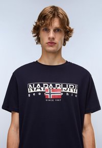 Marineblaue Kurzarm-T-Shirt aus Baumwolle mit einem grafischen Druck, der das Wort "NAPAPIJRI", eine norwegische Flagge und den Text "SINCE 1987" zeigt.