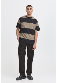 Camisa de manga corta a rayas en beige, negro y tostado; combinada con pantalones negros y zapatos oscuros. Corte clásico y tela suave.