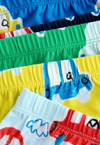 Farverige mønstrede drenge svømmetruser med elastiske waistbands. Designene inkluderer køretøjer på blå, grønne, gule og røde baggrunde.