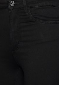Jeans de mezclilla negra con una textura suave, diseño de cinco bolsillos y costuras de contraste. Presenta un cierre estándar con botón y cremallera.