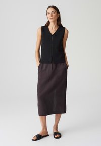 Schwarzes ärmelloses Stricktop mit V-Ausschnitt und Knopfverschluss, kombiniert mit einem dunkelgrauen Leinen-Midi-Rock mit Taschen und einer entspannten Passform. Schwarze Riemchensandalen.