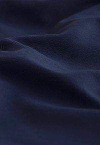 Tela azul marino, textura suave con finas estrías, que cae en suaves ondas, mostrando profundidad y un sutil brillo.