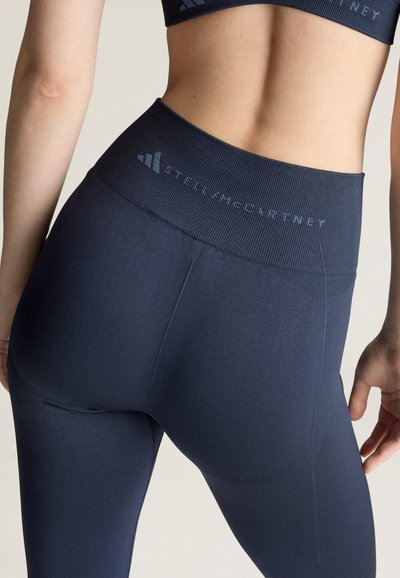Nahaufnahme einer Person, die hochtaillierte marineblaue Sportleggings mit "Stella McCartney"-Logo am Bund trägt.