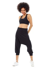 Sujetador deportivo negro y pantalones harem. Tejido suave, cintura elástica, puños fruncidos. Diseño minimalista sin patrones ni logotipos visibles.