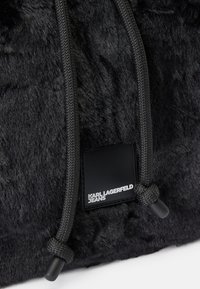 Borsa in finta pelliccia nera con superficie texturizzata, cordini grigi a contrasto e un'etichetta nera rettangolare con la scritta "KARL LAGERFELD JEANS".