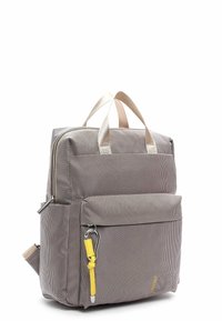 Szary plecak o fakturowanej powierzchni z beżowymi paskami, przednią kieszenią na zamek i żółtą pętlą jako akcentem. Ma kwadratowy kształt i dwa górne uchwyty.