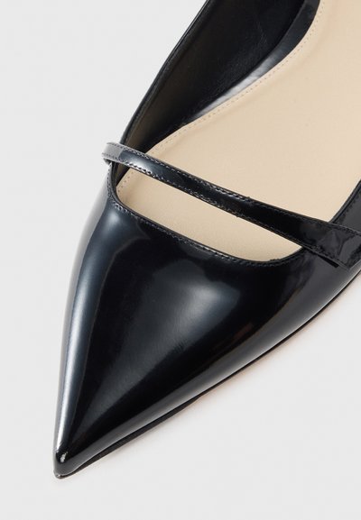 Black patent leather flat shoe with a pointed toe and thin crisscross strap across the vamp; smooth texture with a beige interior lining.