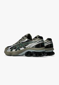 Scarpe da corsa con parte superiore in mesh nera, accenti metallici argento, strisce verdi e nere, e una distintiva suola nera imbottita.