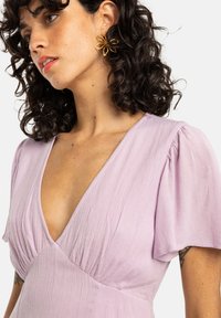 Lavender dress with a deep V-neckline, puffed short sleeves, and textured fabric; gold floral earrings accentuate the look.