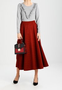 Pull gris avec un col froncé, associé à une jupe rouge texturée. Escarpins noirs et un petit sac à main au design bicolore avec des clous.