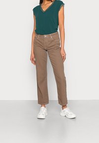 Haut teal avec dentelle, jeans droits marron et baskets blanches. La tenue présente un design simple et un style décontracté.