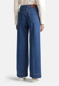 Jeans de mezclilla azul de pierna ancha con cintura alta, costuras claras y dos bolsillos traseros. Incluye un parche de cuero color bronceado en la pretina.