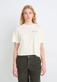 Crème kleurige cropped t-shirt met korte mouwen en "HOUSE OF OBEY" in het zwart gedrukt. Gecombineerd met donkergroene corduroy broek. Soepele stofstructuur.