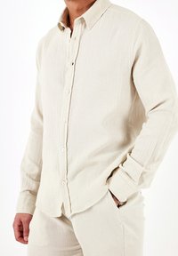 Camicia beige con bottoni realizzata in tessuto testurizzato, dotata di colletto classico, maniche lunghe e chiusura anteriore con bottoni.