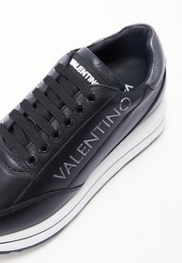 Zwarte leren sneakers met ton-sur-ton veters, witte accenten en een geperst logo op de zijkant. Kenmerkt zich door een stevige witte zool en een gladde textuur.