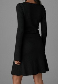 Schwarzes langärmliges Kleid aus geripptem Material, oben figurbetont und an der Taille weit auslaufend, mit einer glatten Textur und einem knielangen Saum.