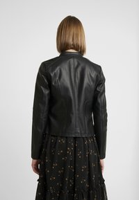 Czarna skórzana kurtka o dopasowanym kroju, gładkiej fakturze i usztywnianych ramionach. Charakteryzuje się szwem z tyłu i krótką długością.