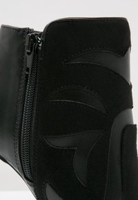 Botín negro hasta el tobillo con un diseño que combina ante texturizado y cuero liso, acentuado con una cremallera lateral y detalles de patrón en capas.