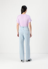 Lavanda majica s zavinutimi kratkimi rokavi, v kombinaciji z svetlolaskastimi širokimi jeans hlačami z teksturo. Obleko dopolnjujejo sproščeni čevlji.