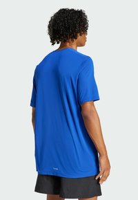 Camisa deportiva azul de manga corta con corte holgado, textura suave, escote redondo y detalle de logo sutil cerca del dobladillo.