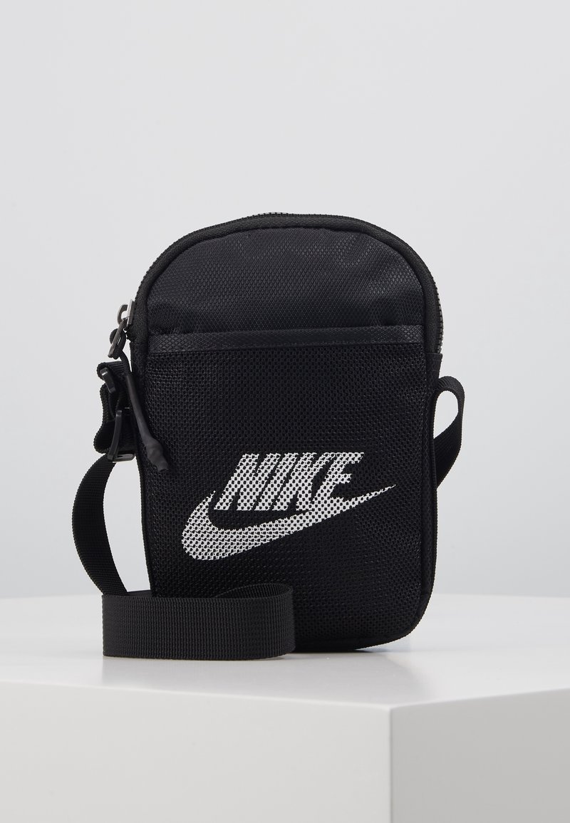 Černá krosová taška Nike s přední síťovanou kapsou, bílým logem a nastavitelným popruhem na bílém povrchu a neutrálním pozadí.