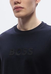 Tengerészkék pamut póló lekerekített nyakkal, a mellkason egy kiemelkedő fekete dombornyomott "BOSS" logóval. Simaságú anyag.