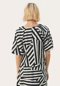 Zwart-wit gestreepte top met korte mouwen, met geometrische patronen en een gebreide stof. Inclusief een knoopsluiting aan de achterkant in het midden.