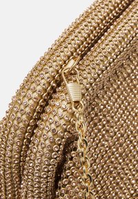 Gros plan sur une pochette en tissu doré recouverte de petits strass, avec une chaîne et un fermoir dorés.