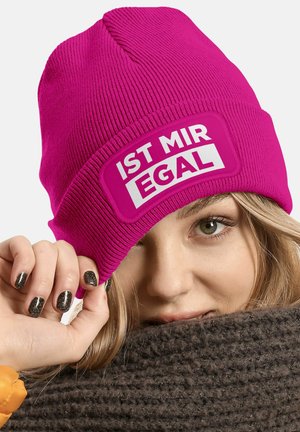 Pink knit beanie with a white rectangular patch displaying the text "IST MIR EGAL." Texture is ribbed, with a snug fit and triangular crown.