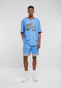 Jersey sportiv din plasă de culoare albastru deschis cu dungi albe verticale, logo negru și șorturi asortate, având accente în dungi alb-negru.