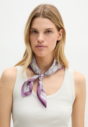 Blonde woman wearing white sleeveless top and purple patterned scarf tied around her neck, facing forward on plain background.