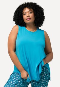 Una blusa sin mangas de color azul claro, hecha de un tejido suave, con una silueta relajada y bolsillos laterales, combinada con leggings de color teal con estampados.