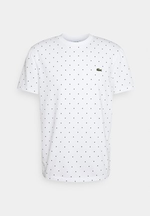 Wit T-shirt met korte mouwen, voorzien van kleine, gelijkmatig verdeelde zwarte polkadots en een klein groen krokodillenlogo op de linkerborst.
