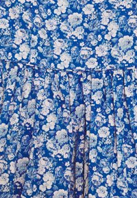 Tela azul con un denso patrón de flores blancas y azul claro, con pliegues recogidos a lo largo de una costura horizontal.