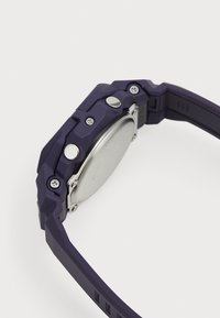 Montre en silicone violette avec un bracelet texturé, des boutons métalliques et un dos de boîtier circulaire en argent, mettant en valeur des vis et des détails visibles.