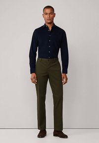 Námořnicky modrá košile na knoflíky s dlouhými rukávy, doplněná tmavě zelenými kalhotami. Outfit dokreslují hnědé boty, které vytvářejí čistý, upravený vzhled.