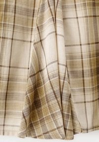 Tissu à carreaux beige et marron avec un tissage doux et texturé, présenté suspendu et drapé avec des plis visibles et des détails du motif.
