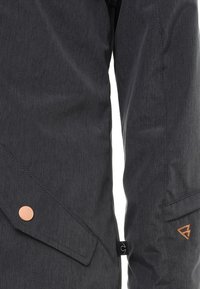 Ciemnoszara kurtka z fakturowanej tkaniny, ukośną kieszenią z miedzianym guzikiem oraz pomarańczowym detalem logo na rękawie.