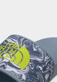 Κοντινή λήψη ενός μονού σανδαλιού slide με λουράκι σε σχέδιο από γρανίτη σε αποχρώσεις του γκρι, άσπρου και μαύρου, με το φωτεινό κίτρινο λογότυπο "The North Face".