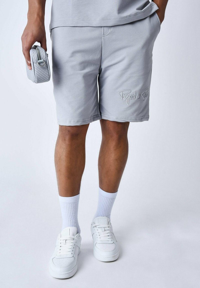 Shorts en coton gris avec un logo brodé, poches latérales et une coupe décontractée, associés à des baskets blanches et des chaussettes mi-mollet.