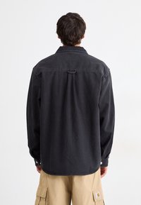 Black denim shirt with a back yoke, long sleeves, buttoned cuffs, and a flat collar; textured fabric with a slightly worn appearance.