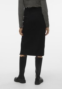 Czarna midi spódnica o dopasowanym kroju, gładkiej fakturze i rozcięciu u dołu, w połączeniu z wysokimi czarnymi botkami i paskowanym swetrem z długim rękawem.