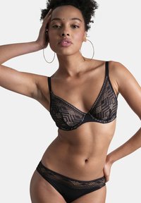 Ensemble de lingerie en dentelle noire comprenant un bralette triangulaire et des culottes assorties, mettant en valeur des motifs géométriques et des textures transparentes.