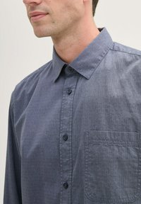 Dunkelblauses Hemd mit Button-Down-Kragen und dezentem Texturmuster, einer Brusttasche links und dunklen Knöpfen.