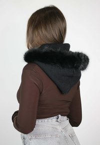 Cappuccio nero lavorato a maglia con bordo in pelliccia sintetica, indossato sopra una camicia marrone a maniche lunghe, caratterizzato da un taglio elegante e jeans grigi a vita alta.