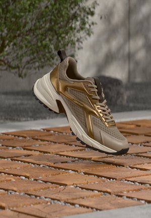 Baskets de sport marron et beige avec des détails en mesh et en cuir flottant au-dessus d'une surface carrelée en bois à l'extérieur.