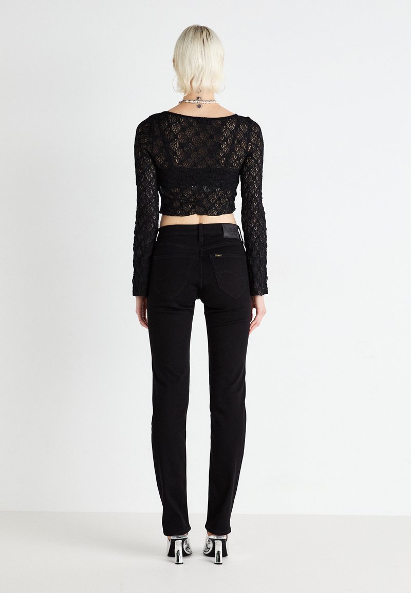 Haut en dentelle noire à manches longues et cropped associé à un pantalon noir taille haute. La tenue présente une silhouette ajustée et un tissu texturé.