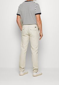 Pantalons en lin beige clair avec une coupe fuselée, deux poches arrière, portés avec un t-shirt rayé marine et blanc et des baskets blanches.