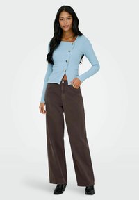 Jasnoniebieska, prążkowana bluzka z długim rękawem, o kwadratowym dekolcie i ozdobnymi guzikami, połączona z szerokimi brązowymi spodniami i czarnymi botkami na obcasie.