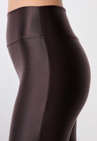 Leggings de cintura alta en un tejido suave de color marrón oscuro. Presentan un diseño elegante, una textura suave y un detalle de costuras mínimas.